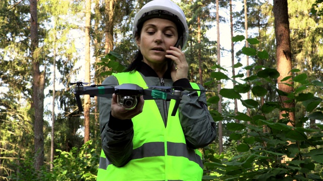在森林里拿着无人机四轴飞行器打电话的女工视频下载