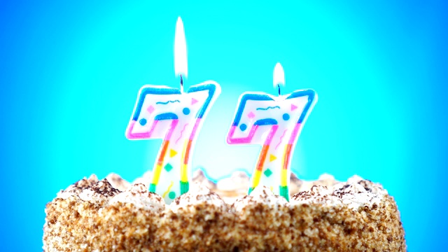 生日蛋糕和燃烧的生日蜡烛。77号。背景的颜色变化视频素材