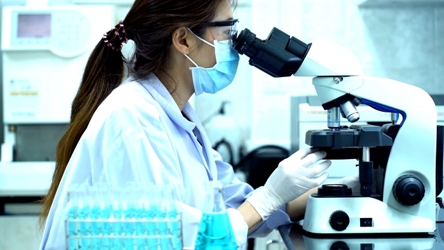 4K女科学家与白色防护服看显微镜和使用吸管填充化学物质到试管在实验室做科学实验视频下载