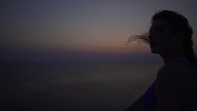 日出前一个美丽的白人女孩的剪影，背景是大海，强风。沉思或准备训练的特写，女运动员视频素材