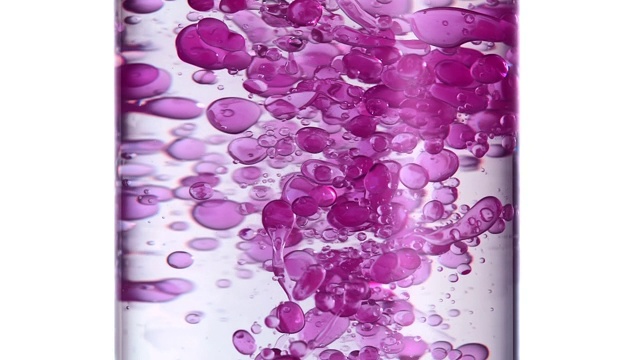近距离观察粉红色液体进入水中变成小气泡并在科学试管中旋转形成一排粉红色气泡的缓慢运动视频下载