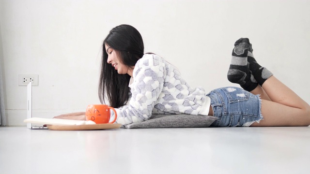 快乐的亚洲女孩躺在地板上，在家里使用笔记本电脑，生活方式在冬天的概念。慢动作镜头。视频下载