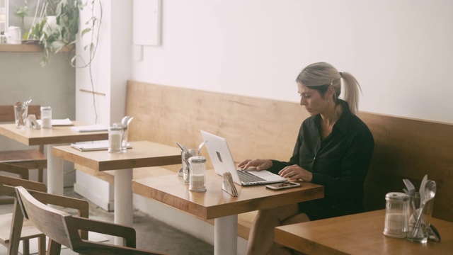 拉丁美洲自由职业者使用智能手机和在咖啡馆用笔记本电脑工作视频素材