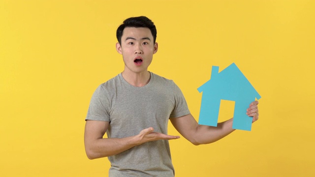 亚洲男子显示蓝色的房子标志在黄色的背景视频下载
