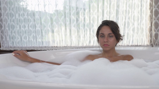 一个年轻女人在泡泡浴中放松的梦幻的正面视图。水疗和美容概念。旋转镜头视频素材