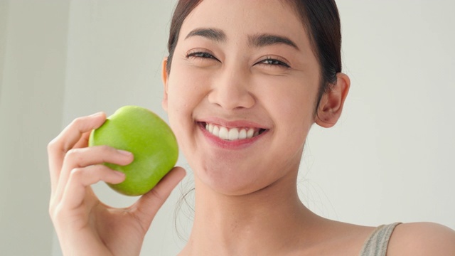 亚洲美丽的女人吃青苹果和微笑与幸福的情绪。减肥的概念，饮食计划，美丽，健康的好处和美丽的牙齿。视频下载