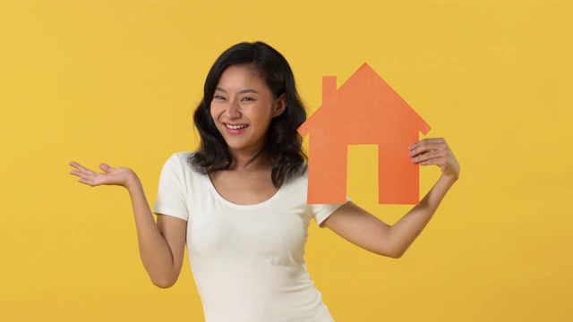 快乐微笑的年轻亚洲妇女展示裁剪出的橙色房子模型视频素材