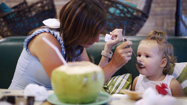 一位母亲和她的宝贝女儿坐在餐厅里共享一顿饭的肖像。第一次给孩子喂食的概念视频素材