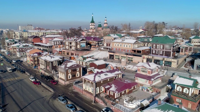 航拍:俄罗斯伊尔库茨克市，无人机在积雪覆盖的建筑旁的街道上接近车辆视频下载