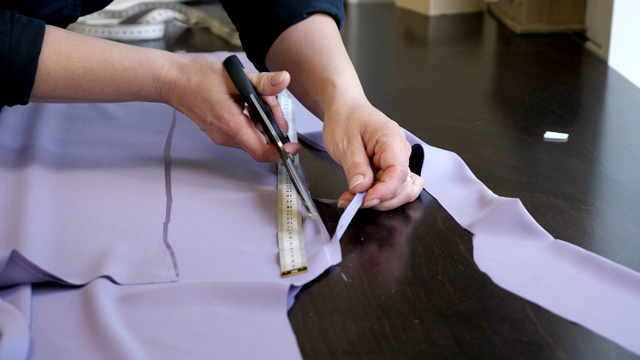 裁缝用剪刀按照粉笔标记的图案裁剪布料，特写手。视频下载