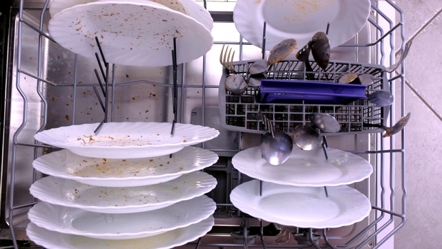 男人的手把一个白色的脏盘子放在洗碗机的篮子里。视频素材