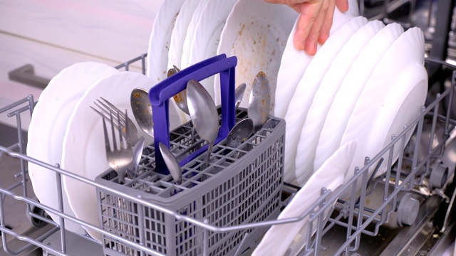 男人的手正在把一个白色的脏盘子放在洗碗机里，然后在厨房里运行它。视频素材