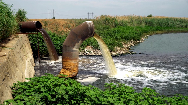 两条生锈的大管道排出的废水以一团团蒸汽的形式汇入河中视频素材