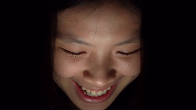 一名年轻的亚洲女子在晚上在家用平板电脑看电影时微笑的照片视频素材