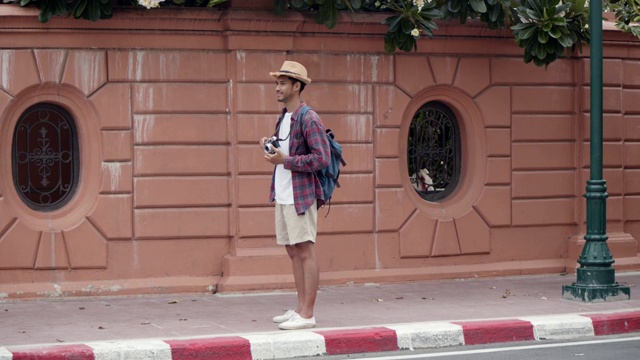 英俊迷人的亚洲游客男子站在泰国街头用相机拍照。亚洲男子博客愉快享受休闲生活方式旅游。视频素材