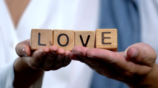夫妻用手掌上的木方制作爱情词，支持和关怀，家庭视频素材