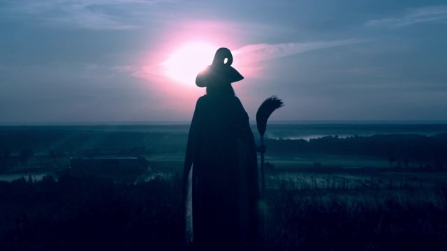 一个穿着女巫服装和扫帚在夜晚摆造型的城市景观的女人视频素材