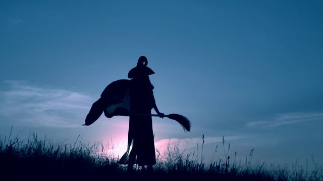戴着帽子和斗篷的女巫拿着扫帚在场上摆姿势视频素材