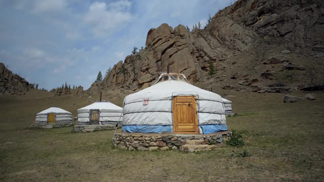 蒙古，乌兰巴托，阳光明媚的日子里，岩石山脉旁的土地上搭建传统的白色蒙古包视频下载