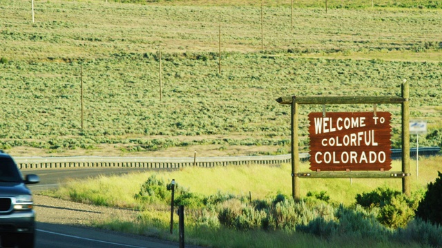 日落时分，70号州际公路上科罗拉多州/犹他州边界上的“欢迎来到五彩缤纷的科罗拉多”州界线标志旁车辆行驶视频素材