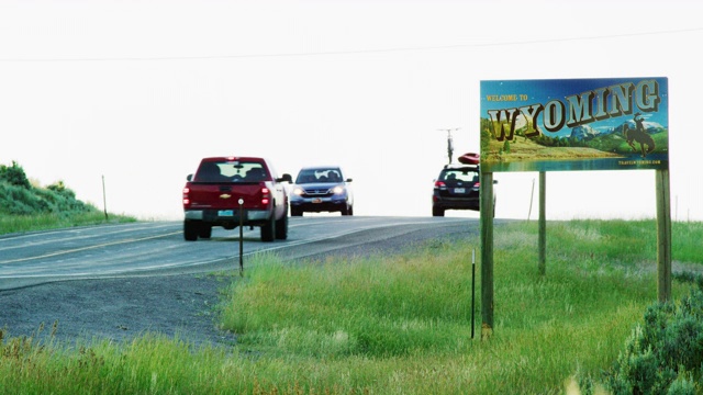 在日落时分，车辆驶过怀俄明州/科罗拉多州边界上的怀俄明州州界线标志视频下载