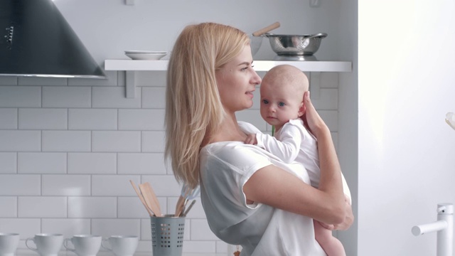 慈爱的母亲握住新生的婴儿女孩的手，年轻的女人温柔地拥抱和亲吻她的孩子在厨房的肖像视频素材