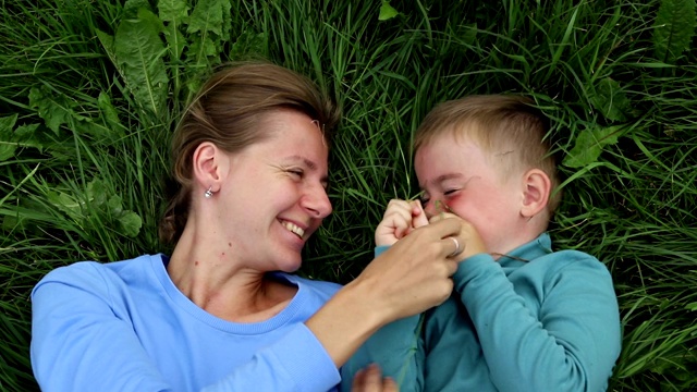 母亲和儿子娱乐的乐趣。妈妈和三岁的儿子躺在草地上玩视频下载