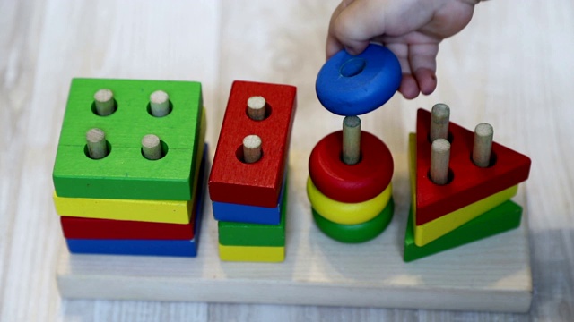 宝宝把一个圆圈放在一个木制构造器上，慢动作。1岁小孩的手和玩具，特写视频素材