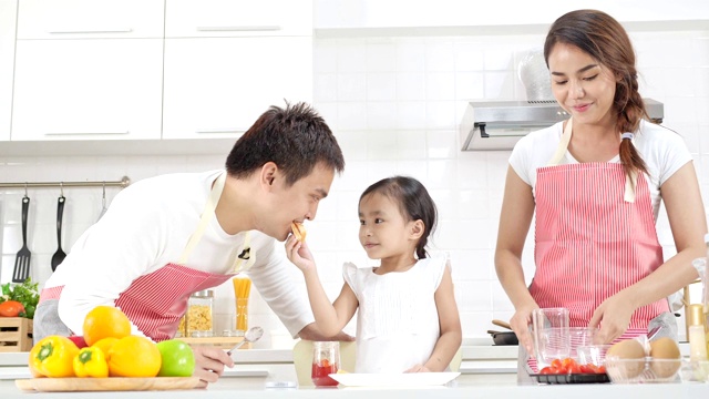 4k慢镜头，年轻的亚洲父亲母亲和女儿快乐和有趣的果酱面包和喂父母在一个现代化的白色厨房。视频下载