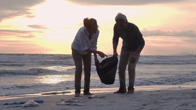 快乐的老两口带着垃圾袋在海滩清扫区域。志愿服务，慈善，清洁，人与生态的概念，高级假期，假期视频下载