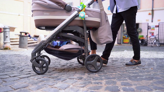 现代舒适的婴儿车与四个小轮子在鹅卵石道路上来回行驶在市中心。快乐的妈妈带着她的小宝宝在户外散步。现代婴儿车的侧视图视频下载