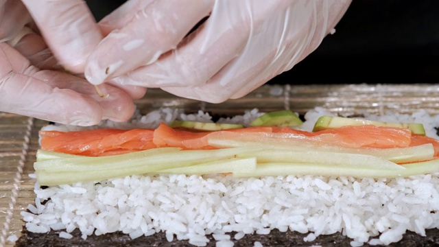 年轻的寿司厨师准备日本寿司卷，米饭，鲑鱼，鳄梨和海苔。餐厅厨房。视频素材