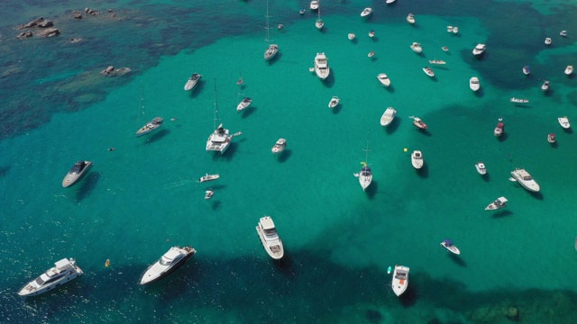 从上面俯瞰，鸟瞰满是船只和豪华游艇的美丽海湾。绿松石般的海水沐浴着绿色和多岩石的海岸。丽莎·鲁贾，翡翠海岸(翡翠海岸)撒丁岛，意大利视频下载