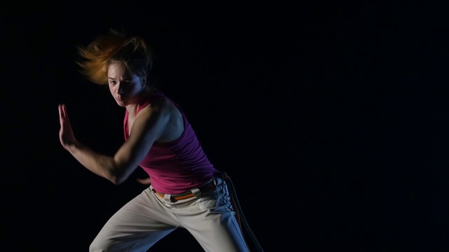 特写，慢镜头，一个女人在演播室黑暗中练习卡波耶拉舞视频下载