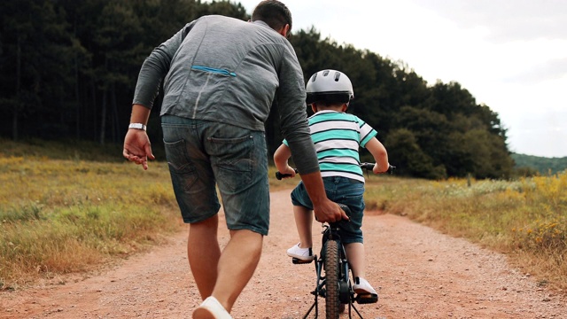 父亲正在公园里教他的小儿子骑自行车视频素材