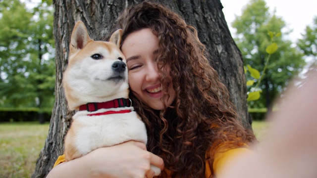 快乐的女孩在公园里与狗狗自拍，宠物抱着相机视频素材
