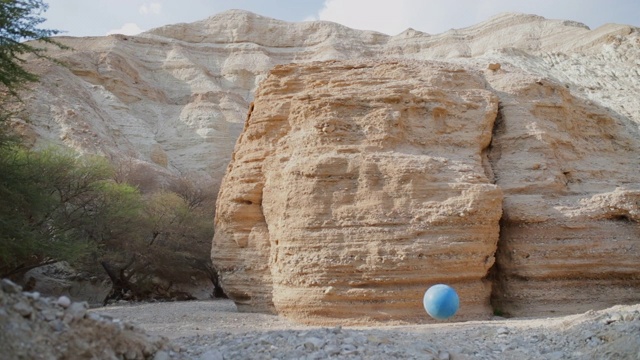 慢动作:一个蓝色的运动球弹跳穿过沙漠的灌木和悬崖-死海，以色列视频素材