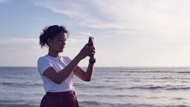 SLO MO拍摄快乐的亚洲女人自拍通过手机在海滩日落视频素材