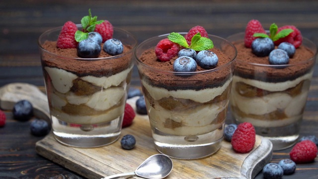 经典的提拉米苏甜点，蓝莓和草莓装在玻璃杯里，放在切菜板上视频素材