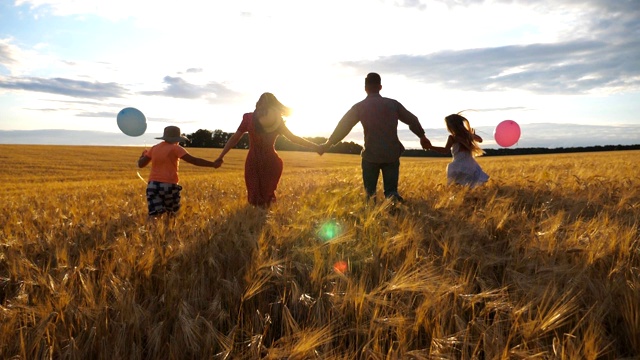 一对年轻的父母带着两个孩子在日落时牵着手跑过麦田。全家在大麦草地上慢跑，一起享受大自然。慢动作视频购买