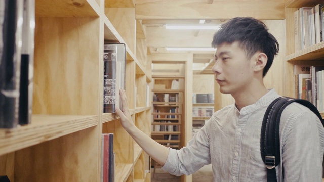 年轻的亚洲男大学生在图书馆找书(慢镜头)视频素材