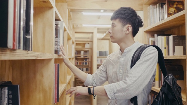 年轻的亚洲男大学生在图书馆找书(慢镜头)视频素材