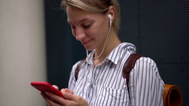 快乐女人戴着耳机听音乐，通过手机应用输入短信的慢动作效果视频素材