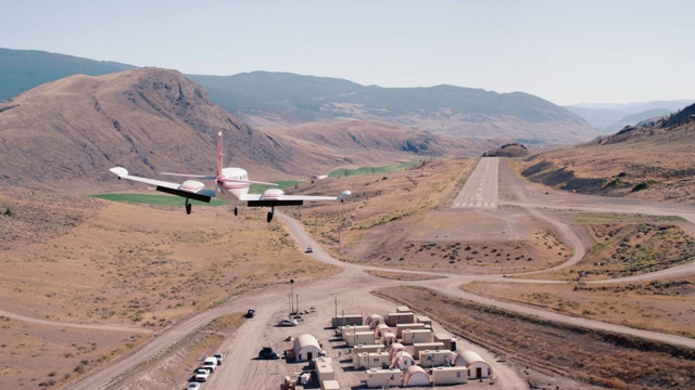 小飞机飞过山脉和沙漠景观的航拍。飞机降落在跑道上。视频下载