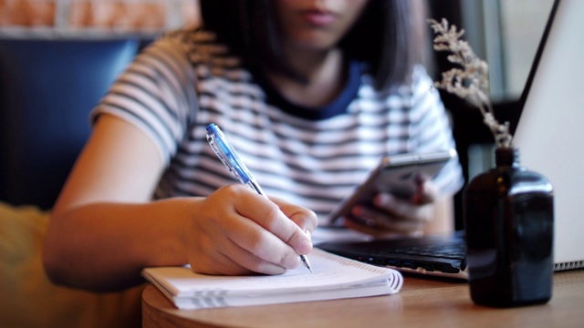 女性工作和书写在笔记本上使用手机，在家工作视频素材