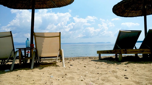 在美丽的沙滩上，柳条沙滩伞和太阳躺椅，蓝天白云，希腊哈尔基迪基视频素材
