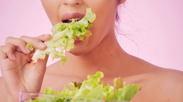 年轻快乐的女人吃着粉色背景上的健康沙拉。清洁平衡的健康食品理念。健康饮食与健身理念。有机食品。医疗保健理念。视频:多样化的肖像视频素材
