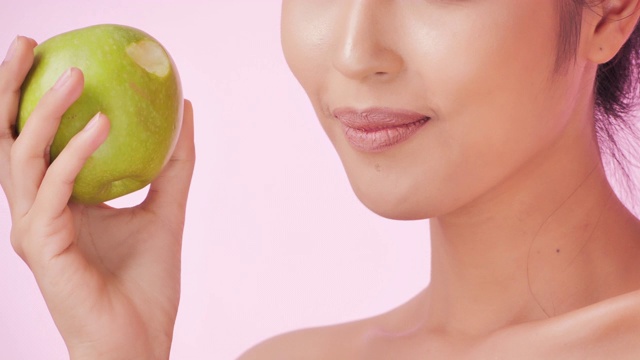 年轻快乐的女人在粉红色的背景下吃苹果。清洁平衡的健康食品理念。健康饮食与健身理念。有机食品。医疗保健理念。视频:多样化的肖像视频素材