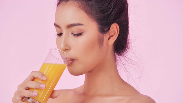 年轻快乐的女人喝橙汁在粉红色的背景。清洁平衡的健康食品理念。健康饮食与健身理念。有机食品。医疗保健理念。视频:多样化的肖像视频素材