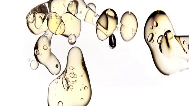 近距离慢动作，清澈的金色液体从右边倒入水中，变成各种大小的气泡漂浮在白色背景上视频素材